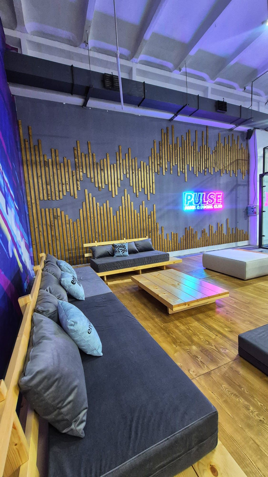 Lounge cu canapele, perne și logo PULSE neon pe perete